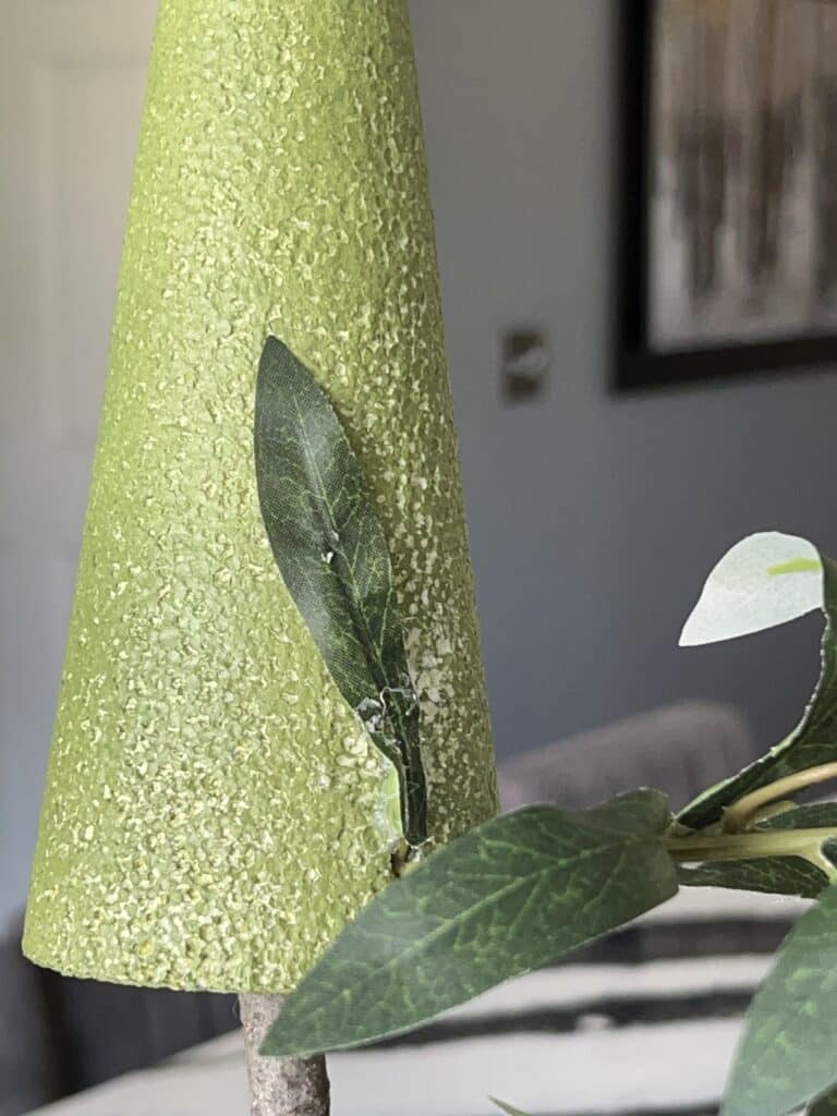 An olive stem that has been pushed into the styrofoam cone and its bottom leaf glued to the cone.