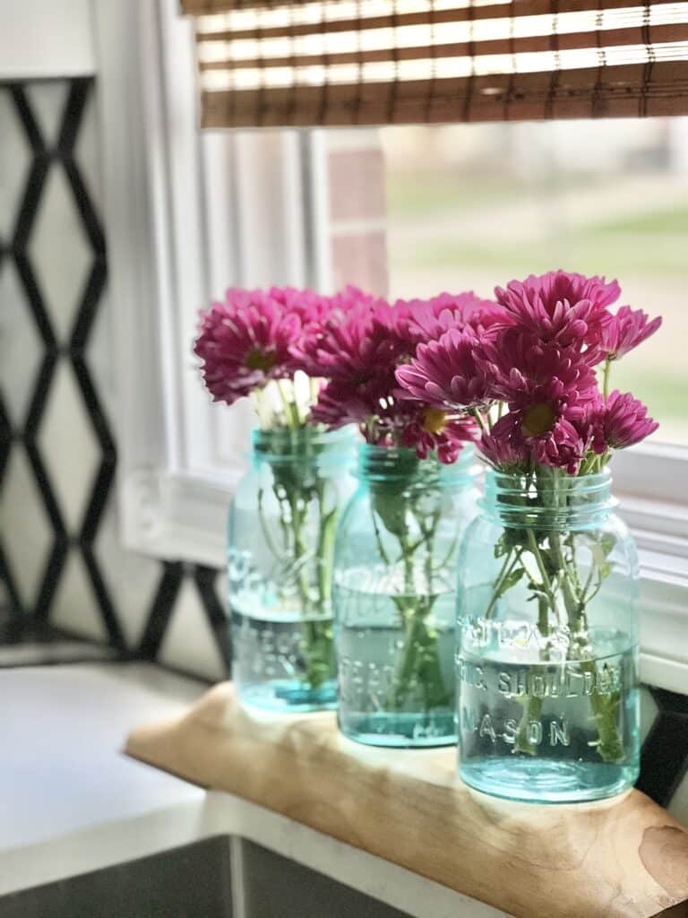 Purple flowers in blue glass mason jars sitting by the kitchen sink.