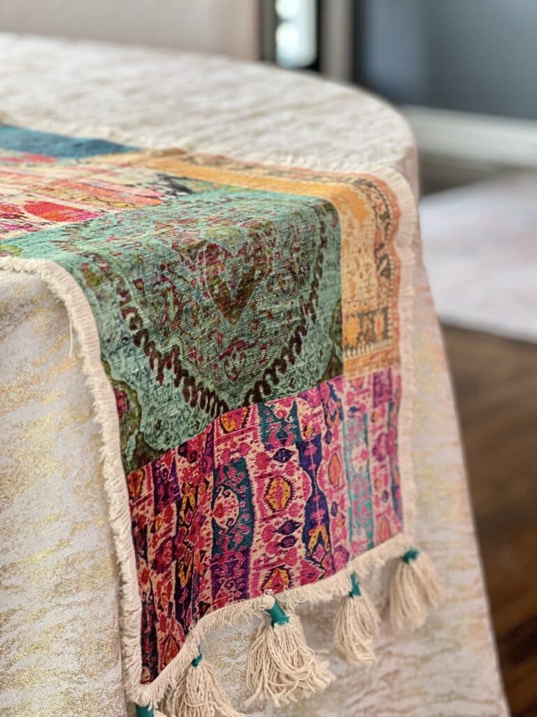 A multi colored table runner draped over a gold and cream tablecloth,.