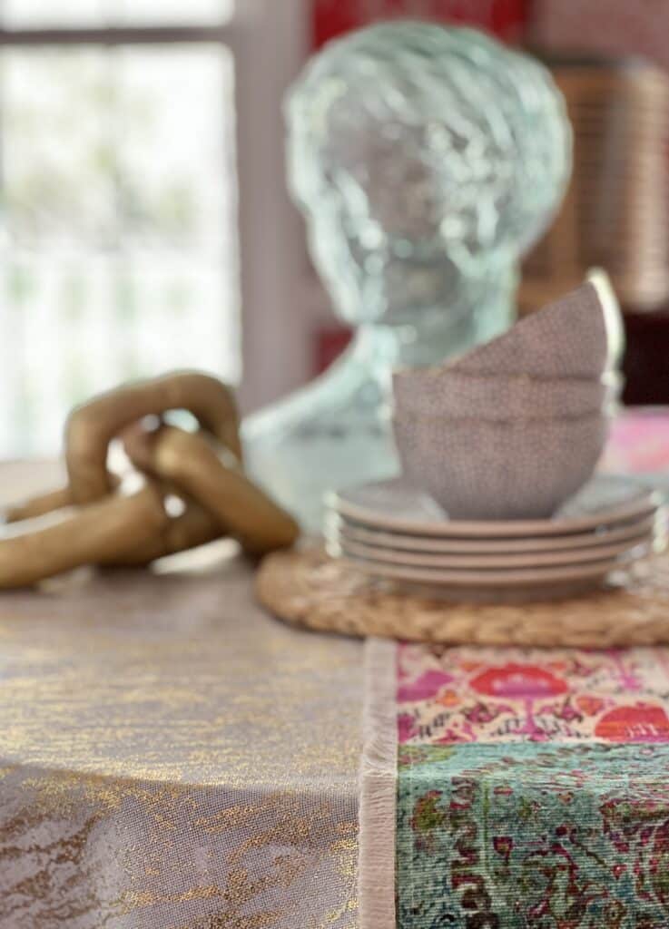 A table runner draped over a tablecloth on a round table with stacks of dishes and bowls.