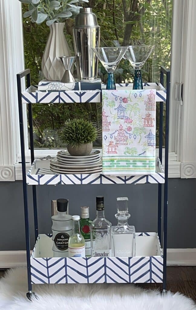 The DIY Ikea bar cart styled with martini glasses, bar cloth, liquor bottles, and a faux plant.