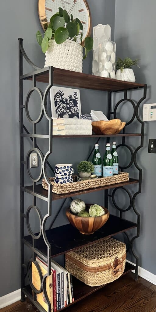 A kitchen bakers rack holding water bottles, plants, and various decorative items.