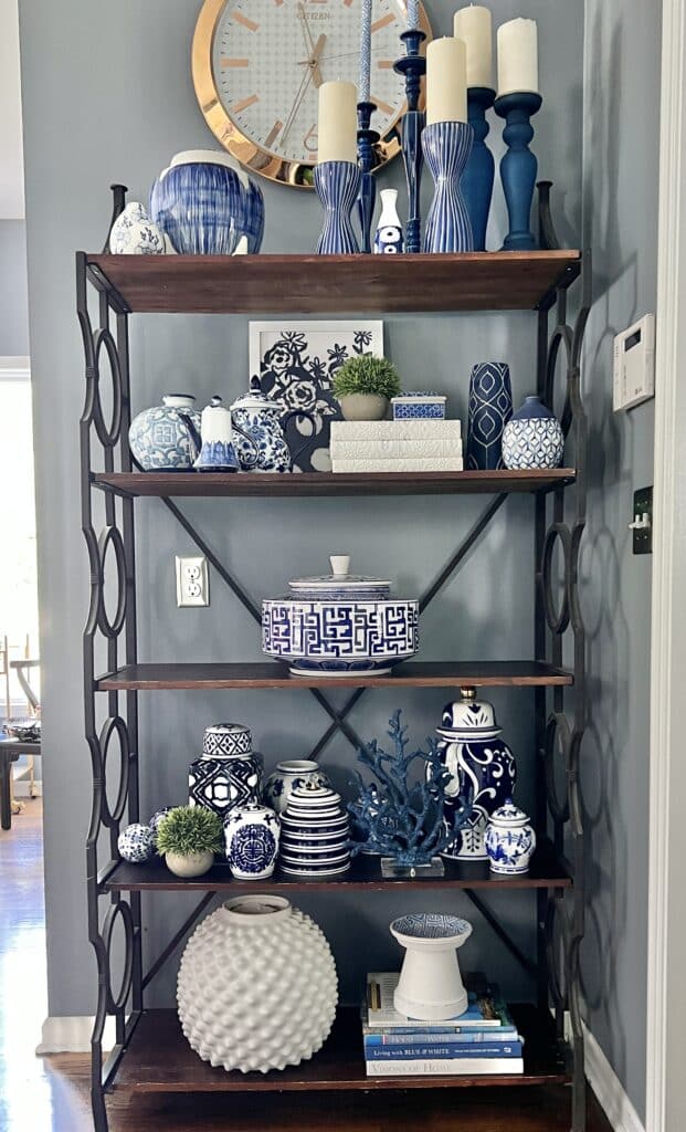 A kitchen bakers rack decorated with blue and white candlesticks, vases, and books.