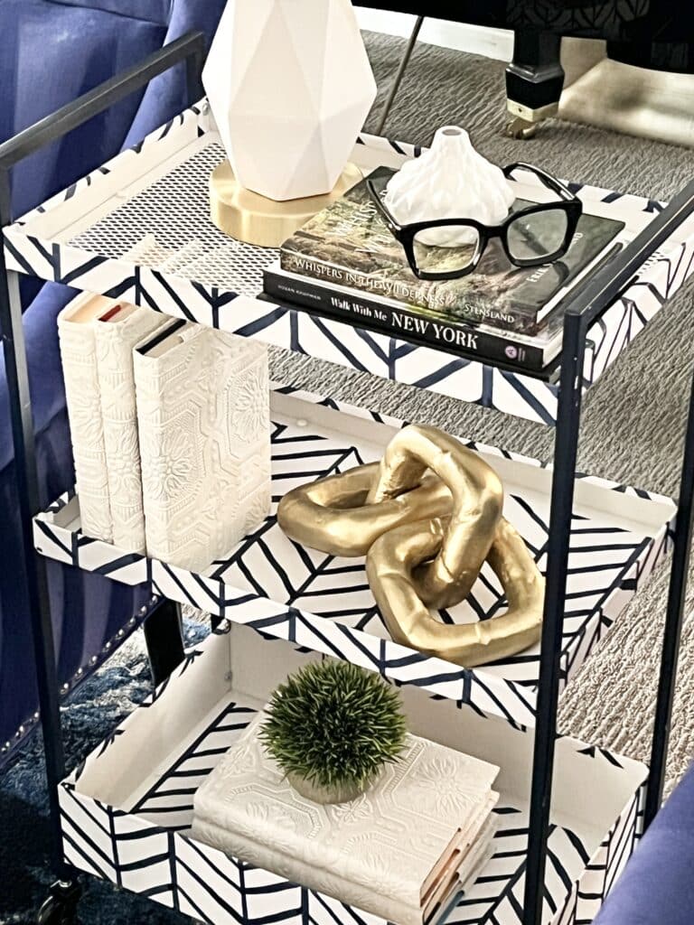 The DIY Ikea bar cart styled as a side table in a living room with books, plants, and a small white lamp.