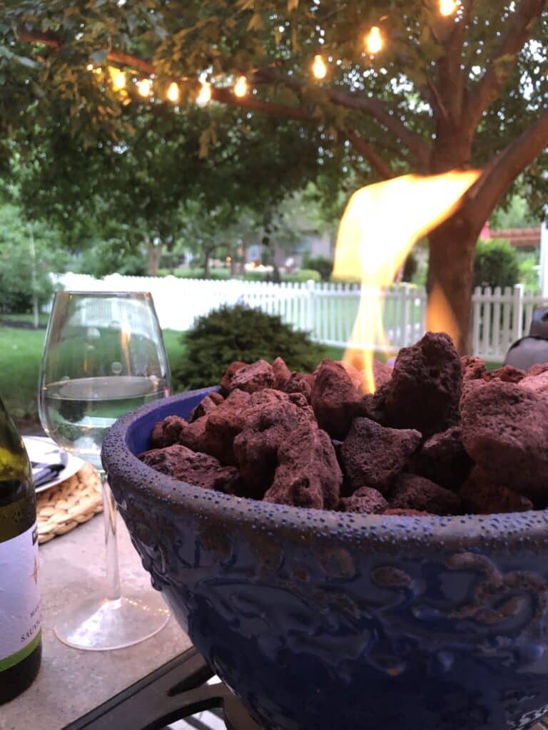 A DIY tabletop fire pit made from a blue pot sits on top of a patio table with a glass of wine beside it.