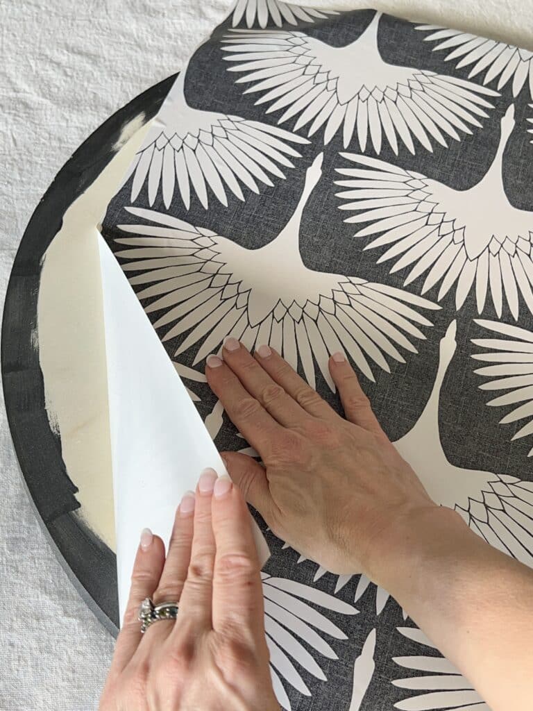 Applying black and white peel and stick wallpaper to the wood disk.