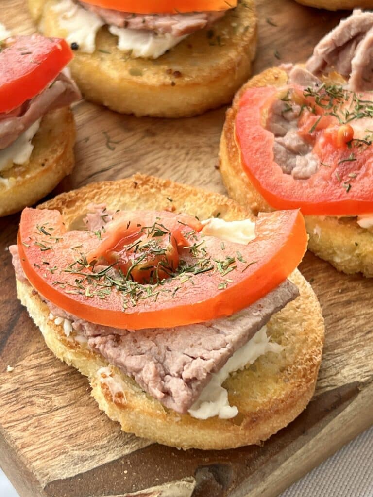 Tomato slices and dill weed are added to the top of the bruschetta appetizer.