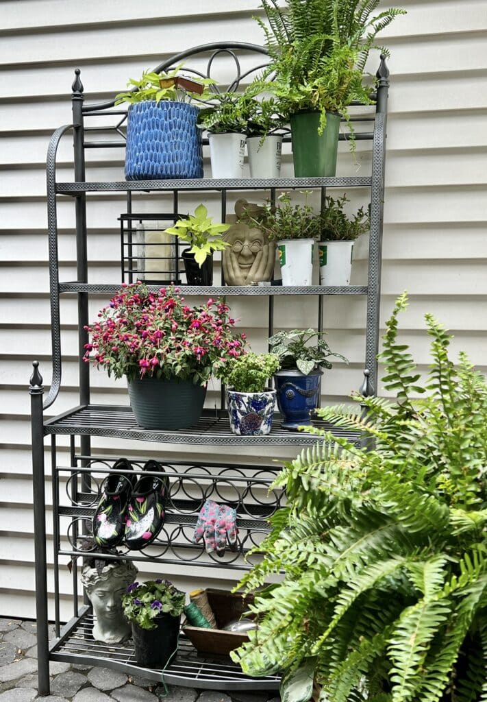 A kitchen bakers rack sitting on an outdoor patio holding colorful plants and flowers.