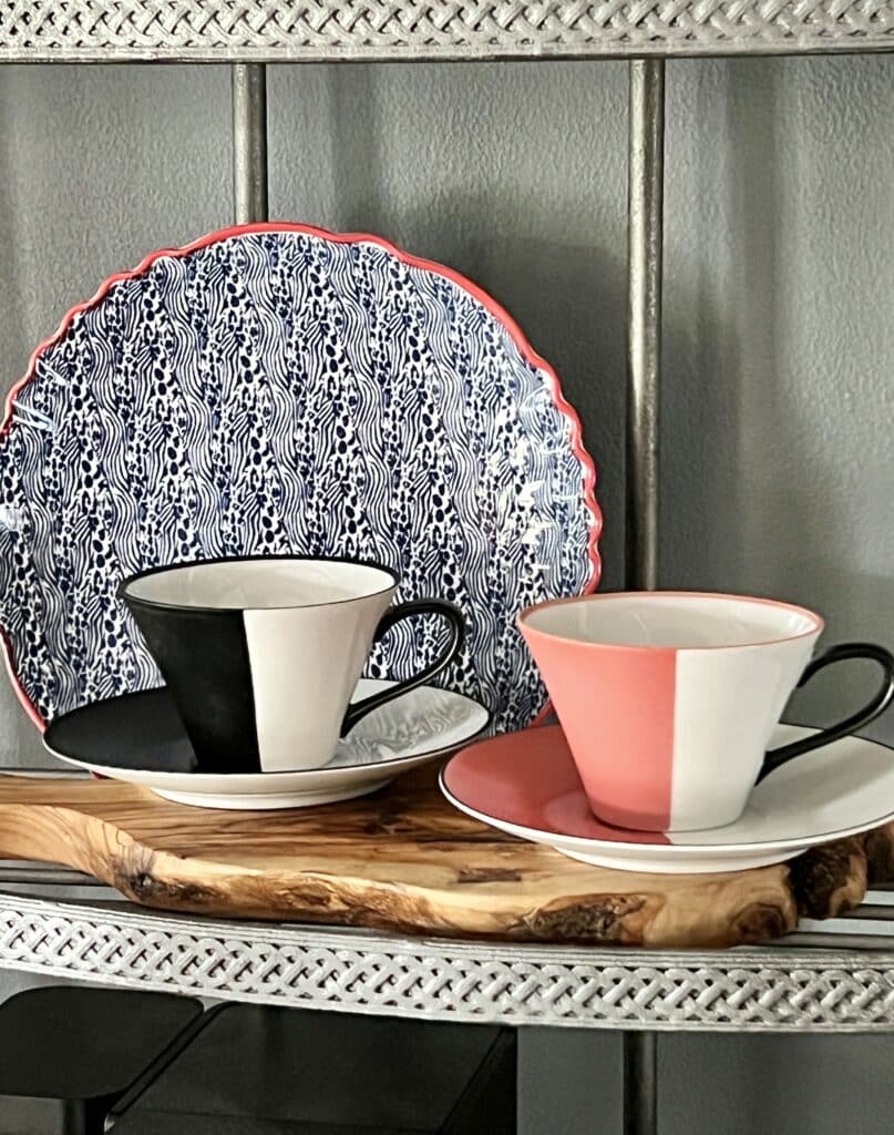 A blue and white decorative plate propped along the back of a shelf with two coffee cups sitting in front.