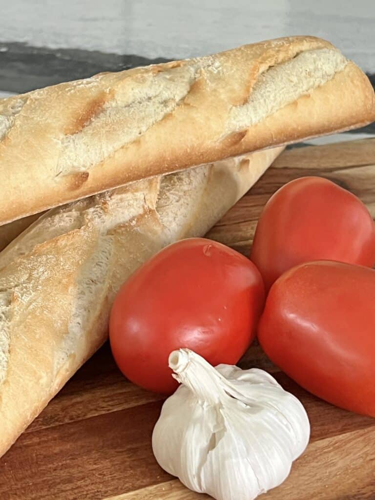 A french bread baguette with Roma tomatoes and a head of garlic.