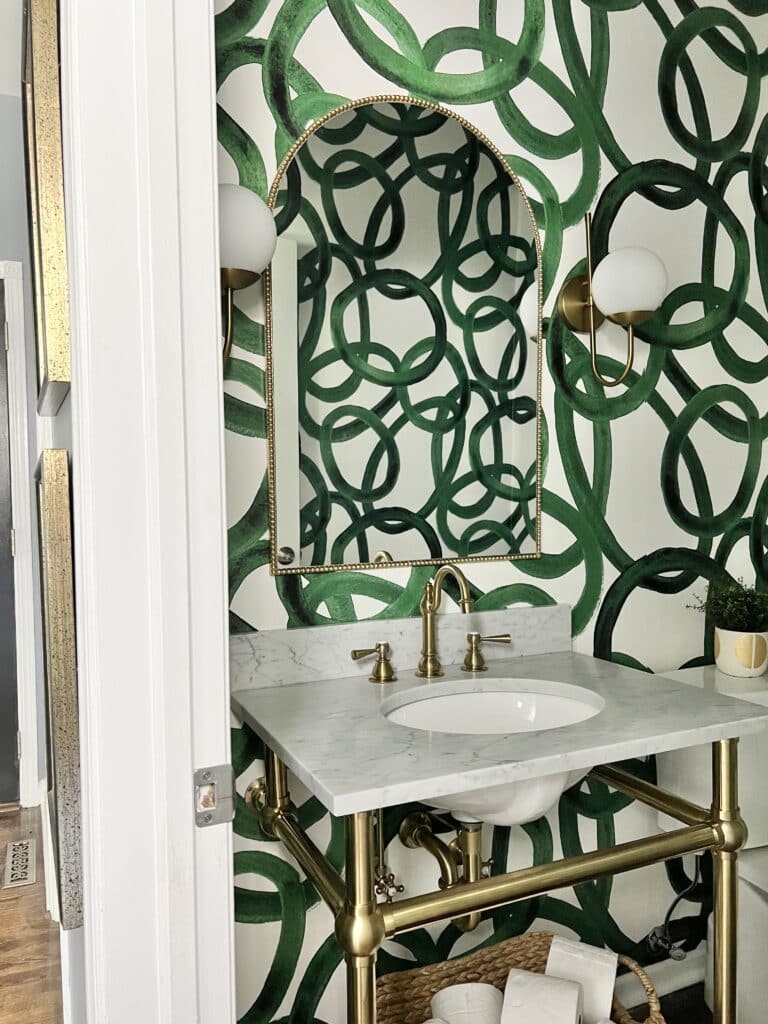 Half bath makeover ideas shown with green and white wallpaper, a marble top vanity sink, and gold metal accents.