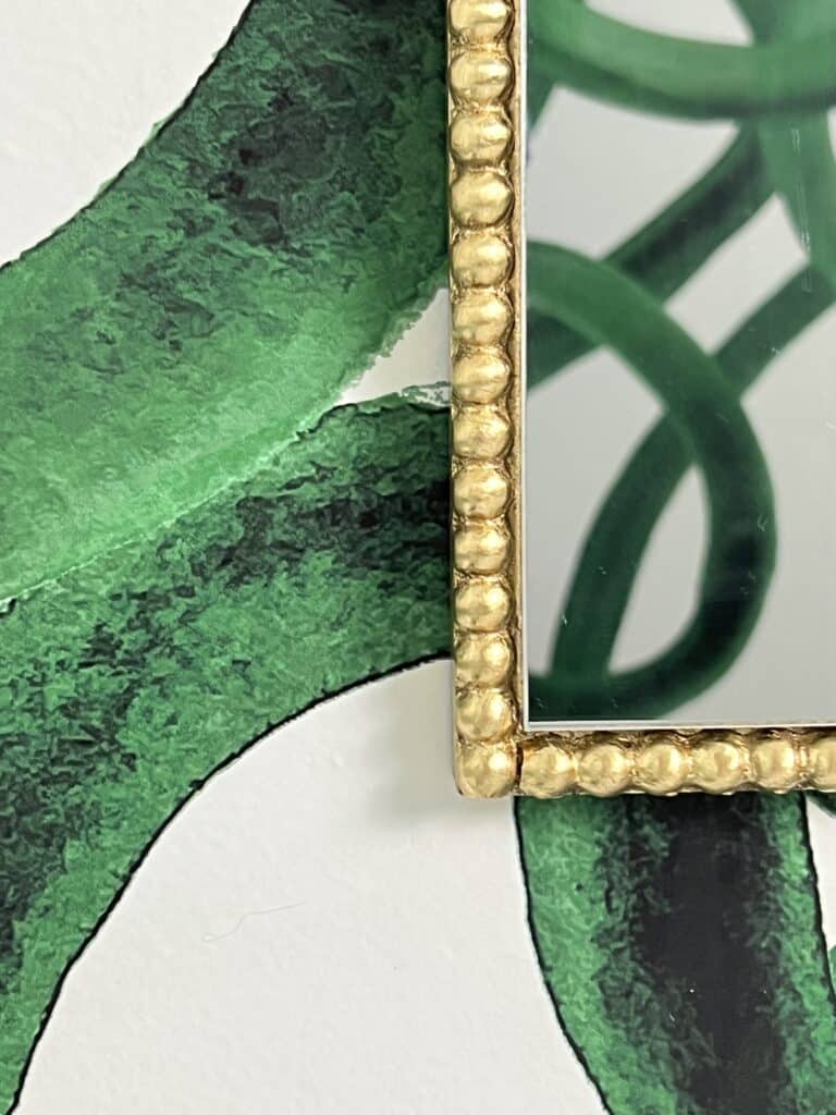 A gold beaded mirror frames against green and white wallpaper.