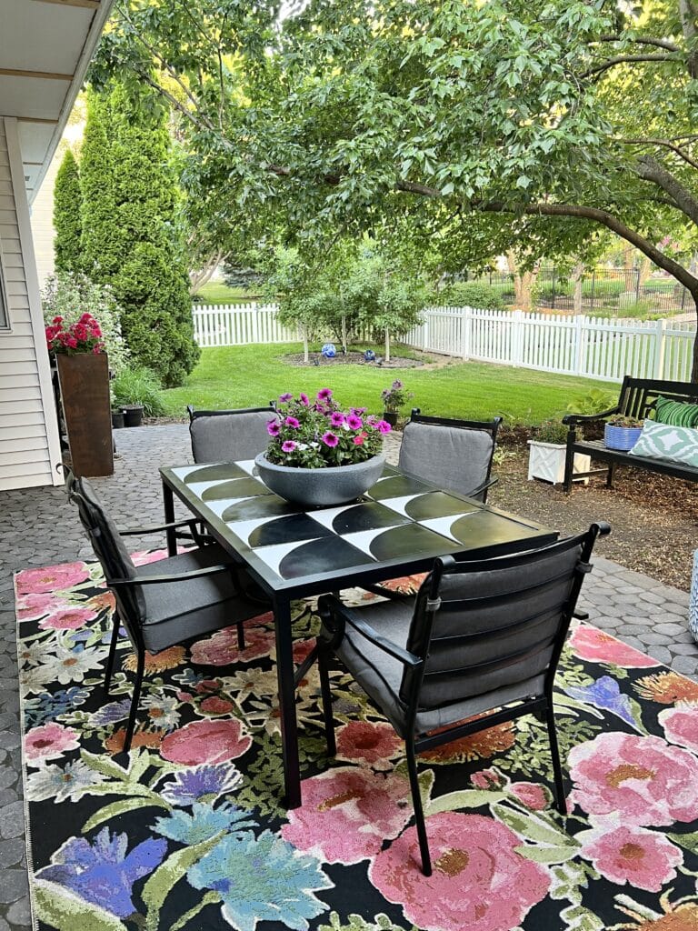 A cobblestone patio with a dining table and chairs and potted plants.