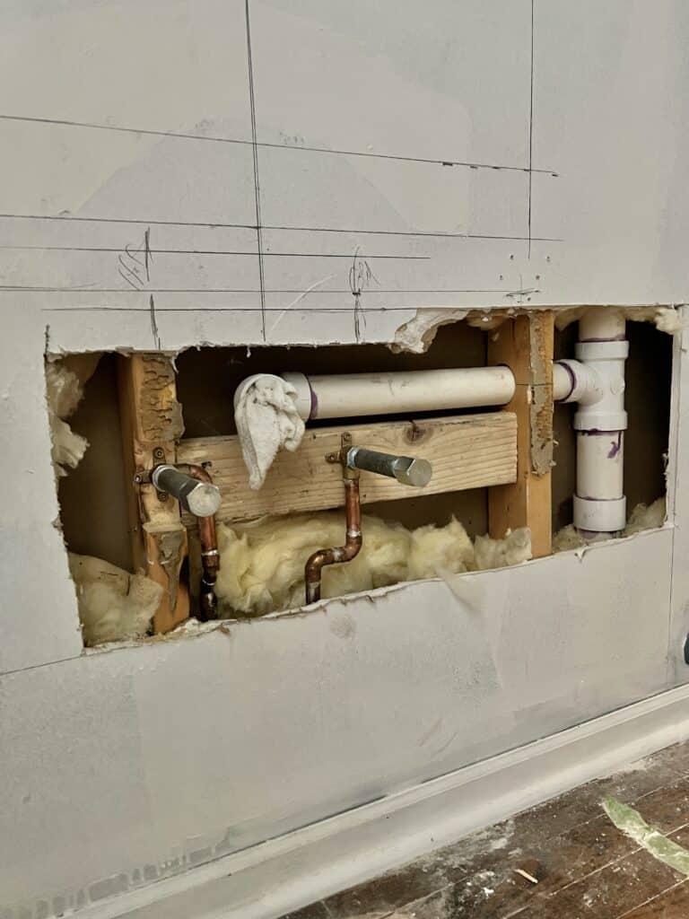 A hole in the half bath wall after the plumber prepared the room for the new sink.