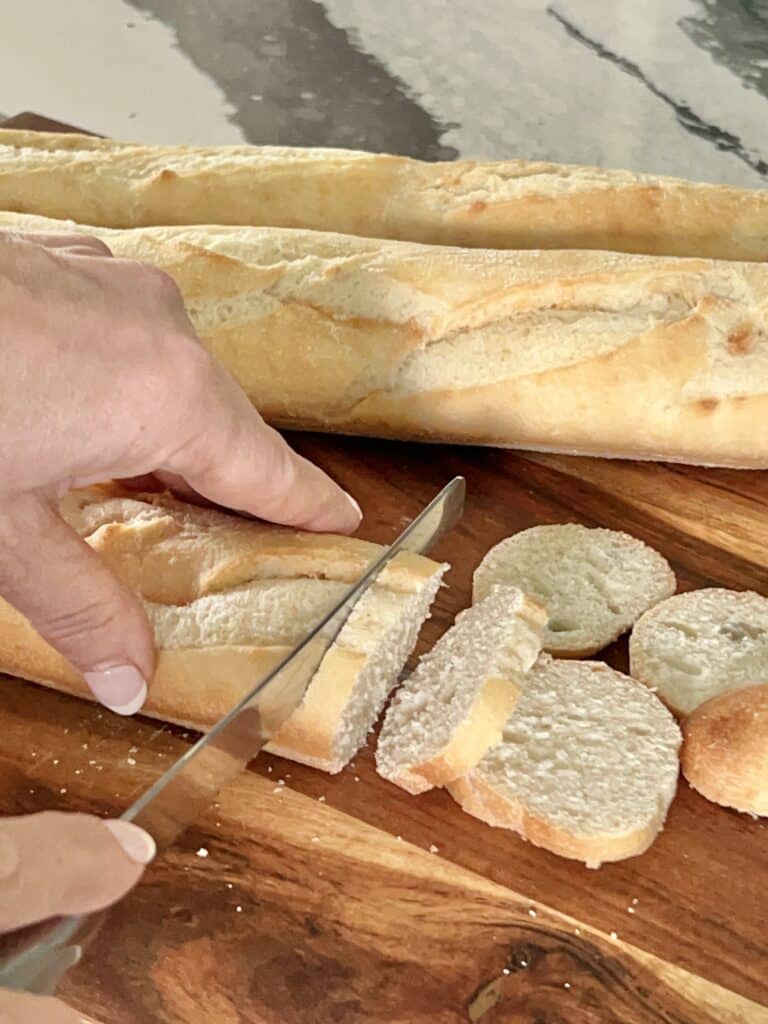 Slicing the baguette bread into thin slices with a serrated knife.