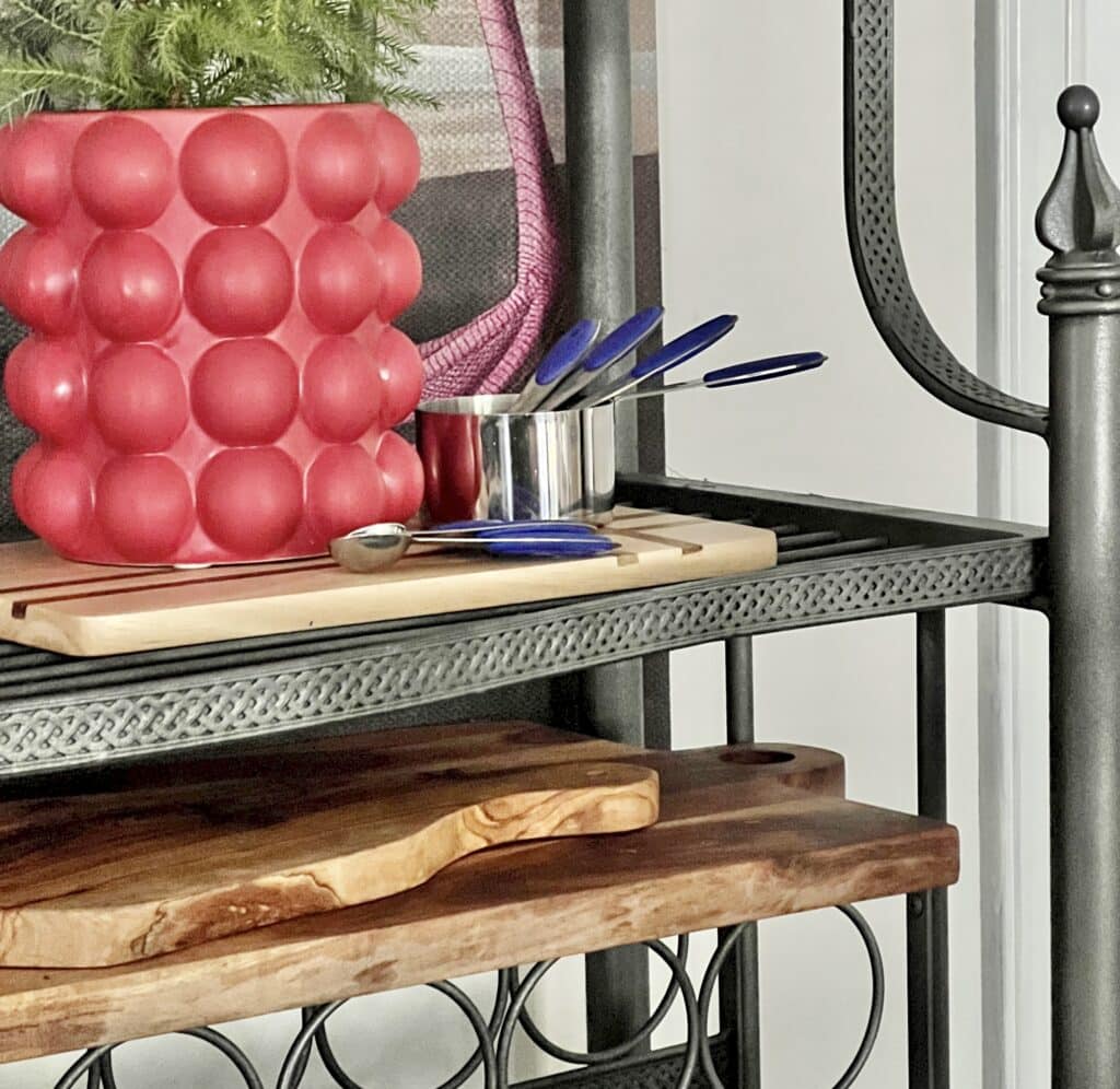 Wood cutting board displayed horizontally on the shelf of a kitchen bakers rack.