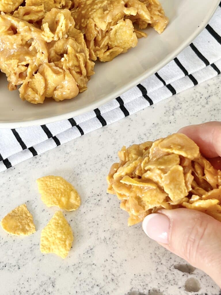 cereal cookie recipes: Grabbing a peanut butter corn flake cookie from a white plate.