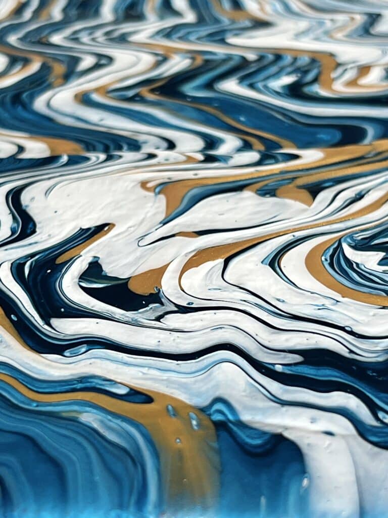 DIY abstract wall art: A close view of the blue, white, and gold curvy paint effect of the paint pour on the canvas.