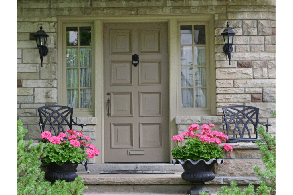 Plants good for a covered porch: Two pots of pink geraniums flank the front door on a covered front porch.