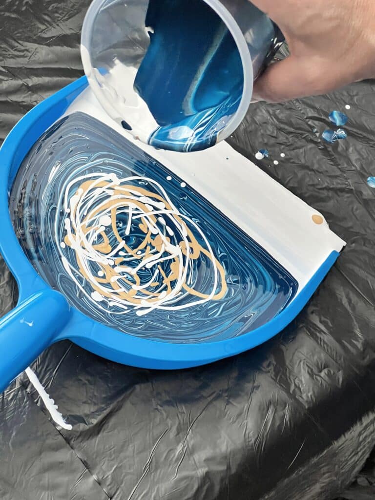 Pouring the layered blue, white, and gold paint onto the dustpan.