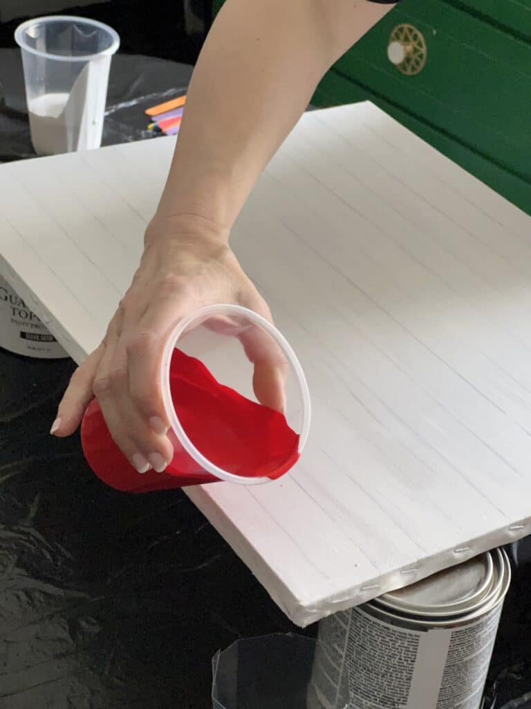 Pouring the first stripe of red paint on the white canvas.