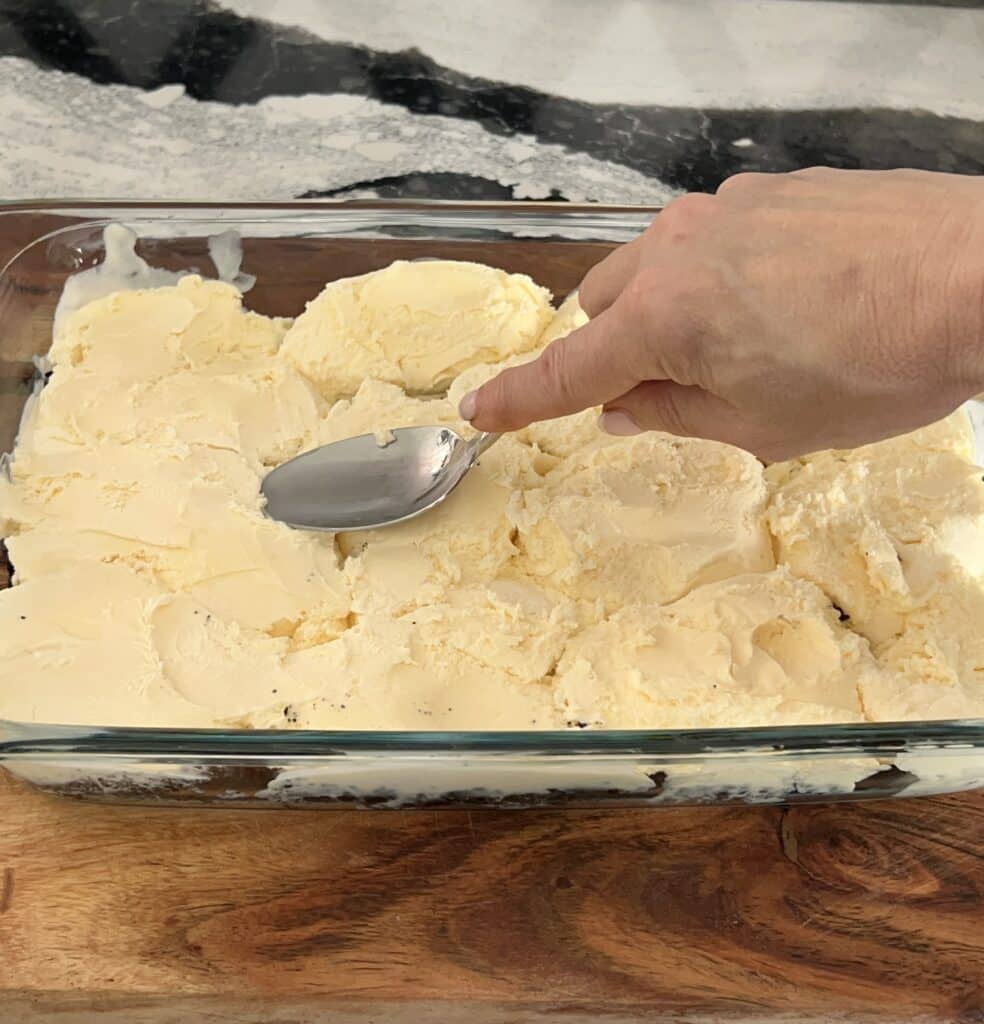 Using the back of a spoon to spread a layer of vanilla ice cream over the cookie crust.