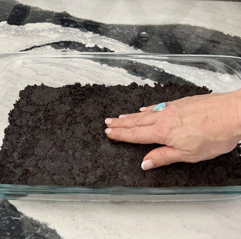 Pressing the Buster Bar recipe cookie crumbs into the corners of a glass 9 x 13 pan.