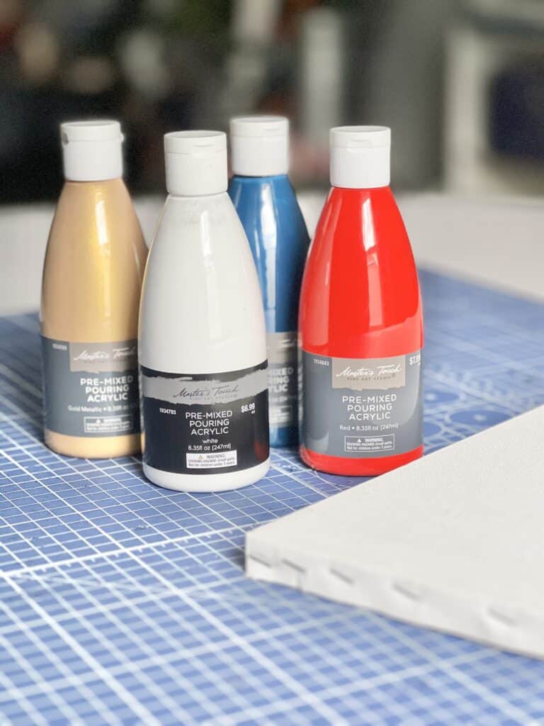 DIY abstract wall art: Bottles of pourable paint in gold, white, blue, and red colors.