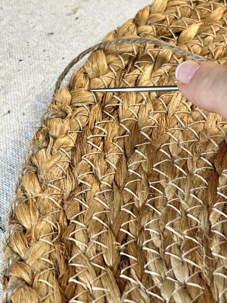 Using an upholstery needle to hand sew two jute placemats together to create a DIY boho pillow.