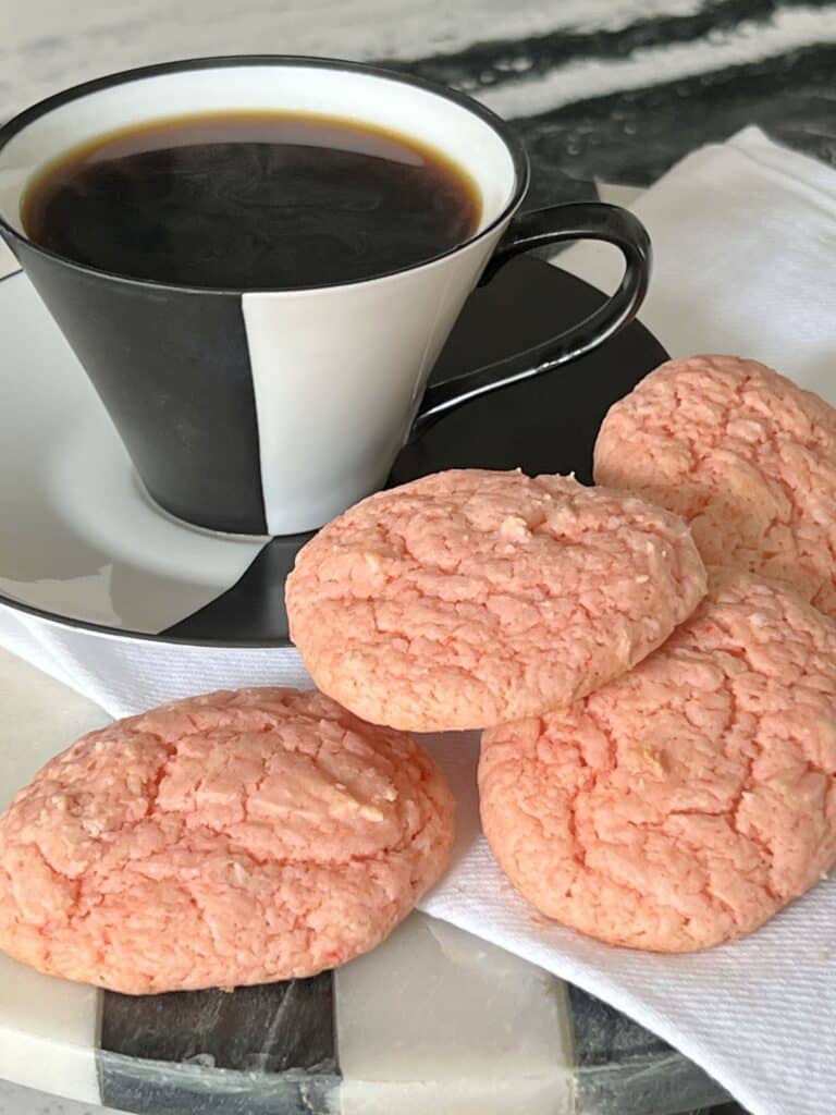 A cup of black coffee with pink strawberry cookies.