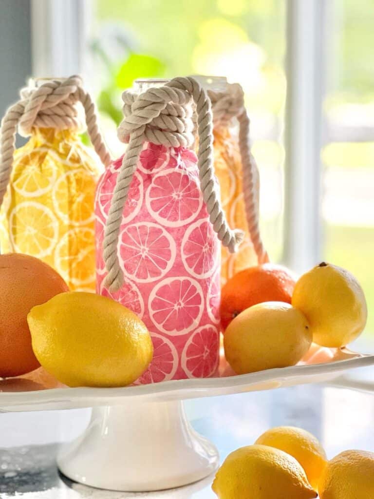 A white pedestal try filled with decoupage bottles and lemons.