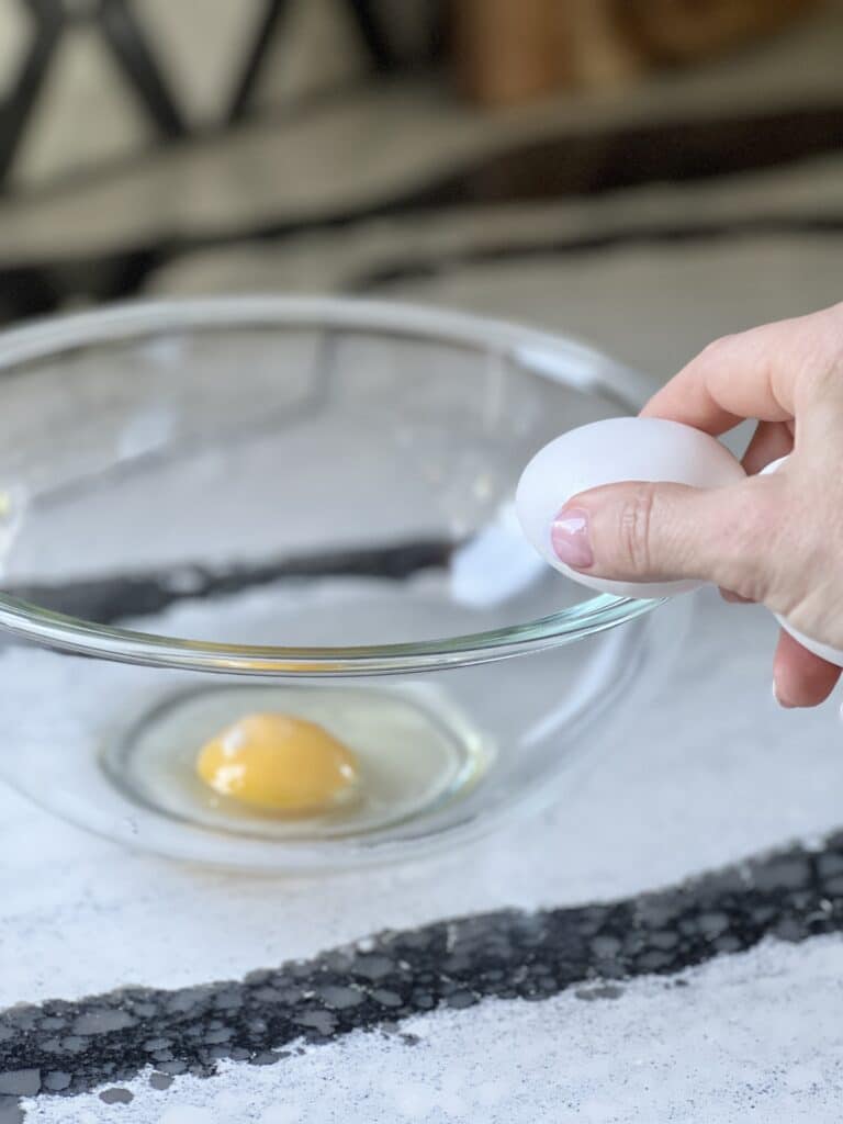 3 ingredient strawberry cake cookies: Cracking an egg into a bowl.