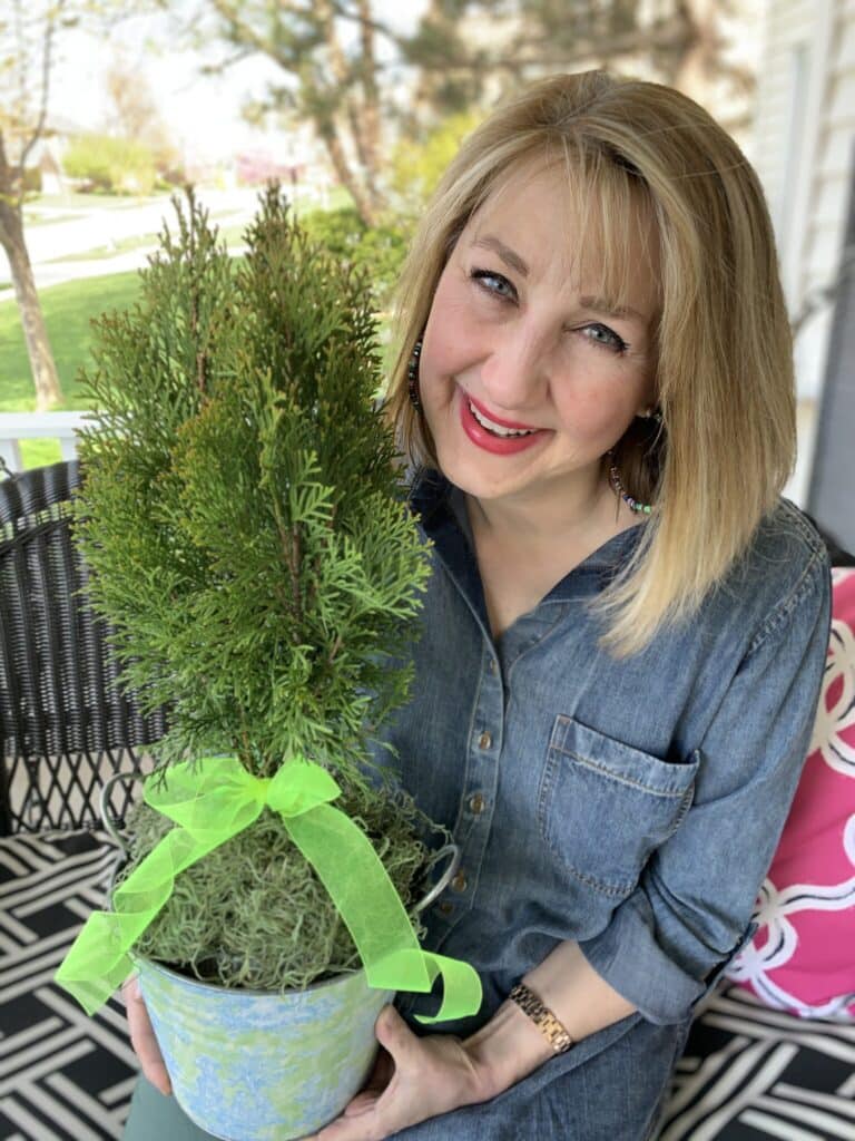 35 Thoughtful New Neighbor Housewarming Gift Ideas: Missy holding a small tree gift-wrapped in a bucket with ribbon.