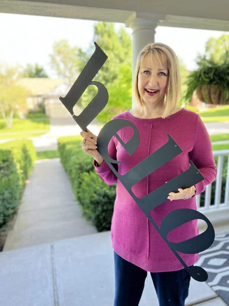 35 Thoughtful New Neighbor Housewarming Gift Ideas: Missy holding a metal "hello" sign.