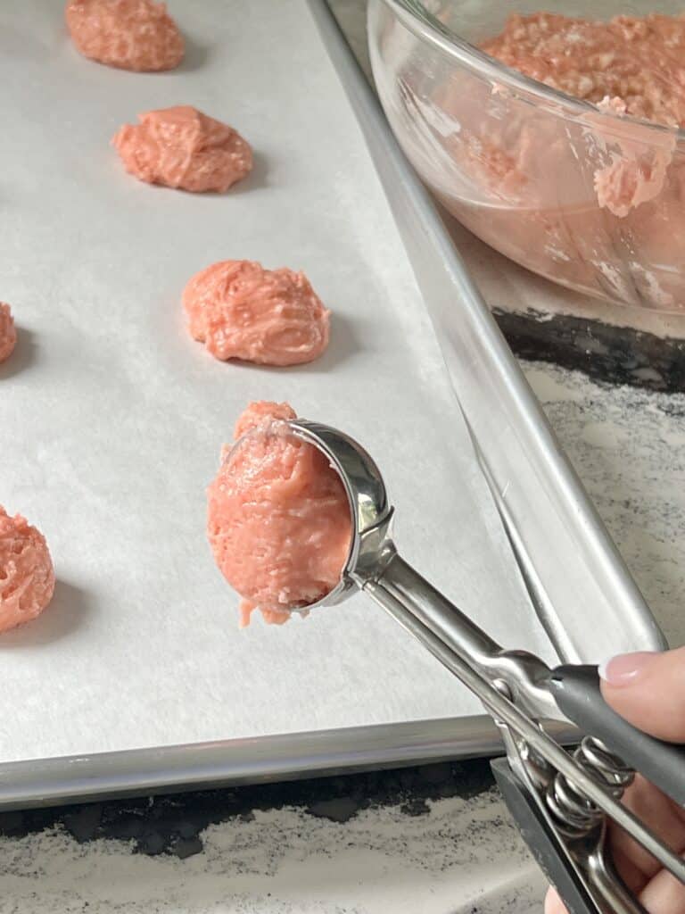 Scooping cookie batter onto a parchment paper lined baking sheet.