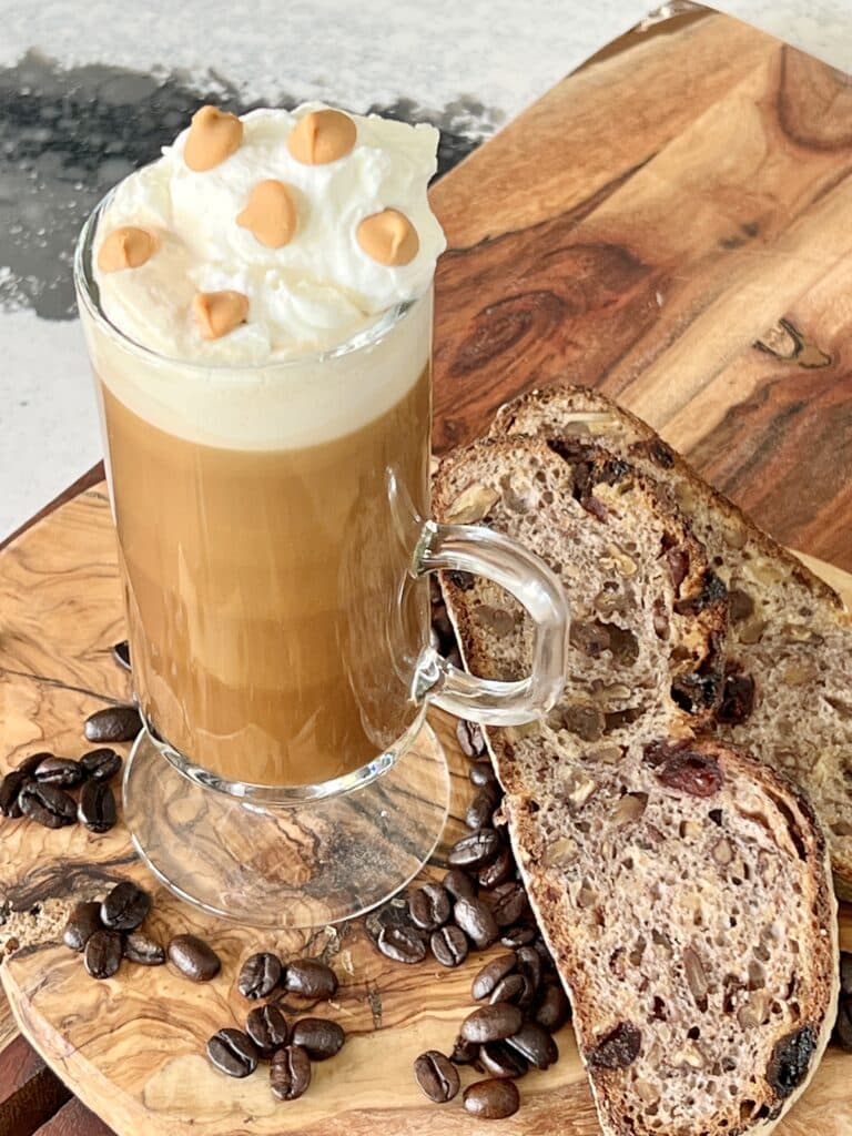 A smoked butterscotch latte recipe in a glass mug and sitting on a wood cutting board.