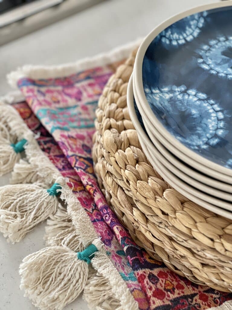 A table runner and stacks of woven placemats and dishes are helpful for how to decorate a kitchen island.