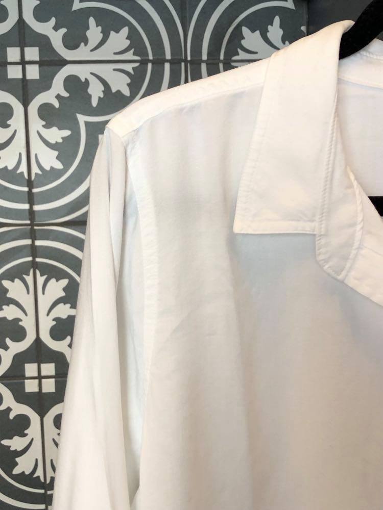 A white shirt hanging in a closet.