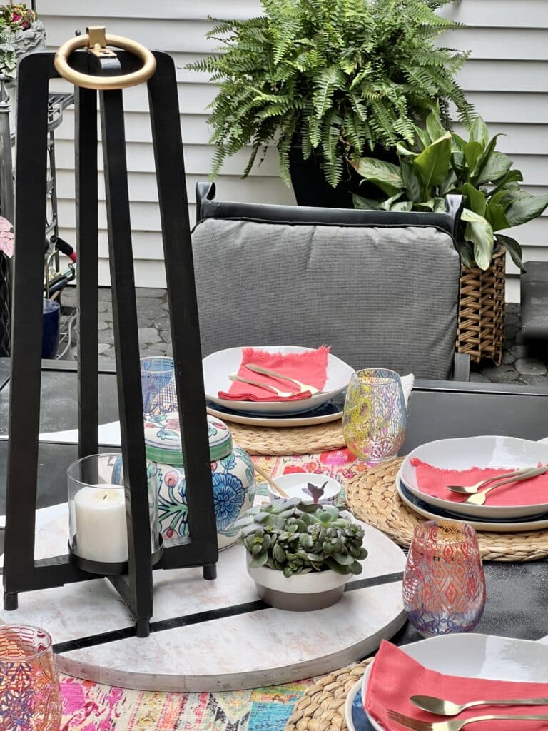 everyday table centerpiece ideas: A tall black lantern sitting on a wood cutting and sitting on a patio table.