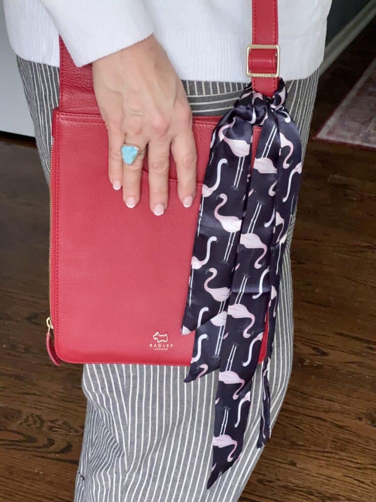 A red crossbody bag with a flamingo patterned twilly scarf.
