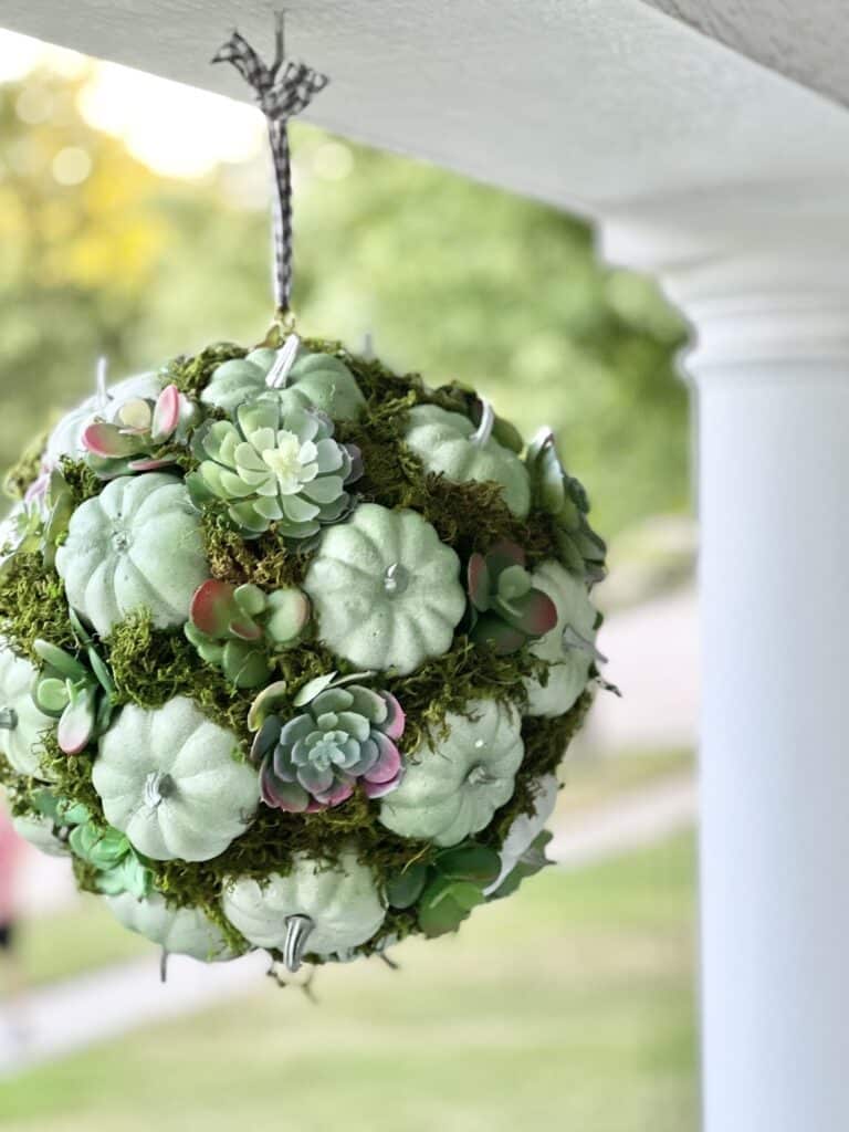 A pumpkin kissing ball hanging on a front porch.