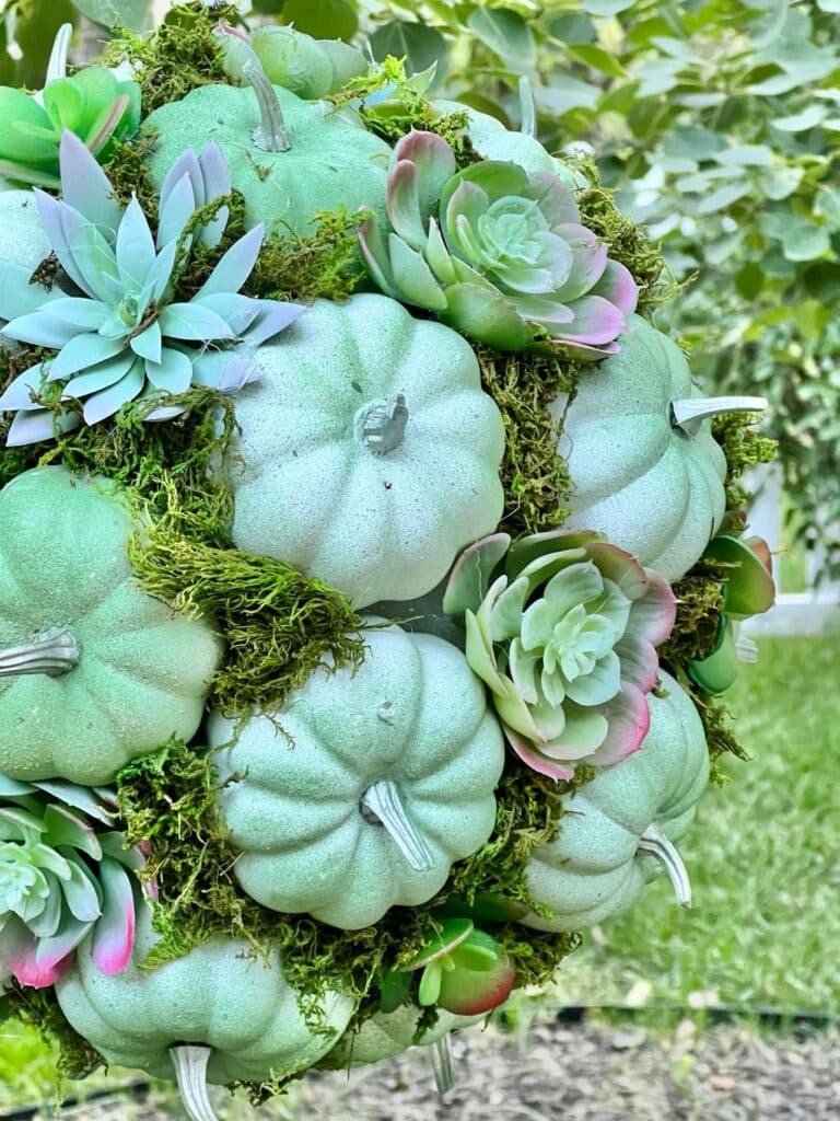 small faux pumpkins and succulents on a diy pumpkin kissing ball hanging outdoors for fall decoration.