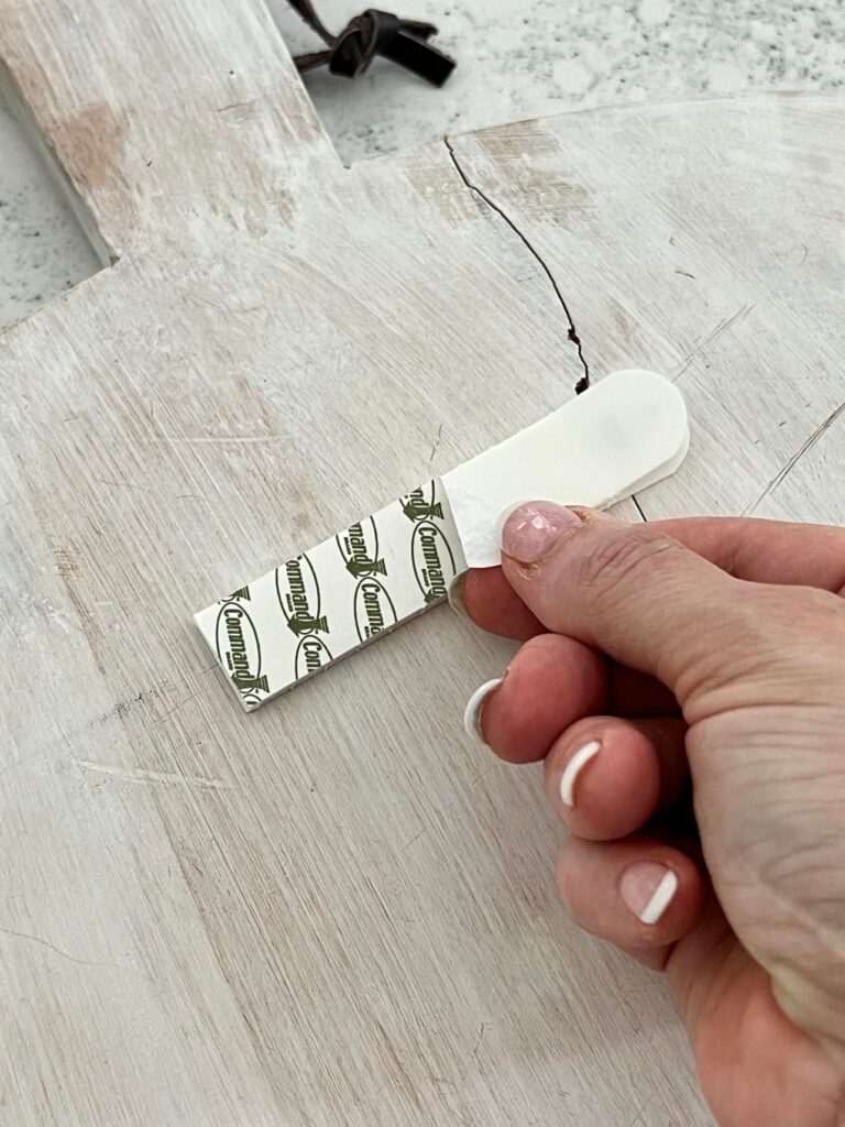 how to hang cutting board on wall: Peeling away the cover of the adhesive strip.