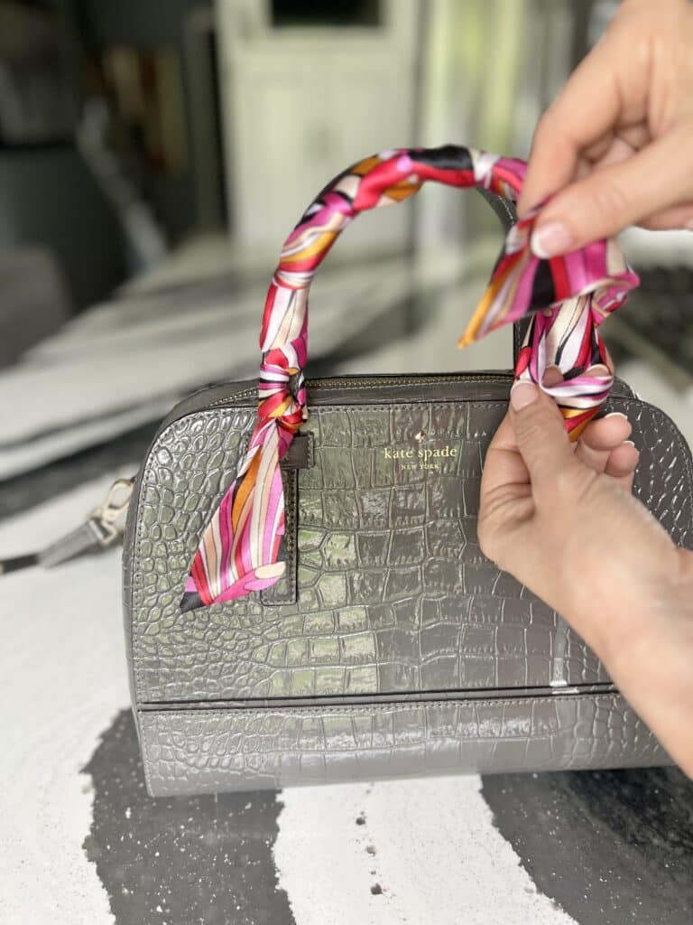 Tying a knot after wrapping a purse handle with a scarf.