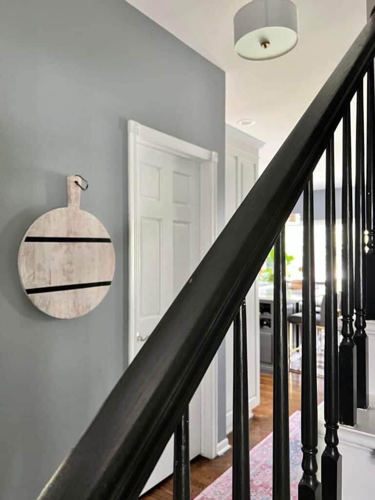 how to hang cutting board on wall: A wood cutting board hanging on the wall by the kitchen stairwell.