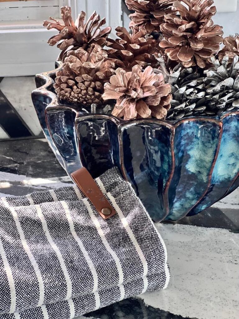 kitchen fall decor ideas: Rose gold spray painted pine cones sitting in aa navy blue pottery bowl.
