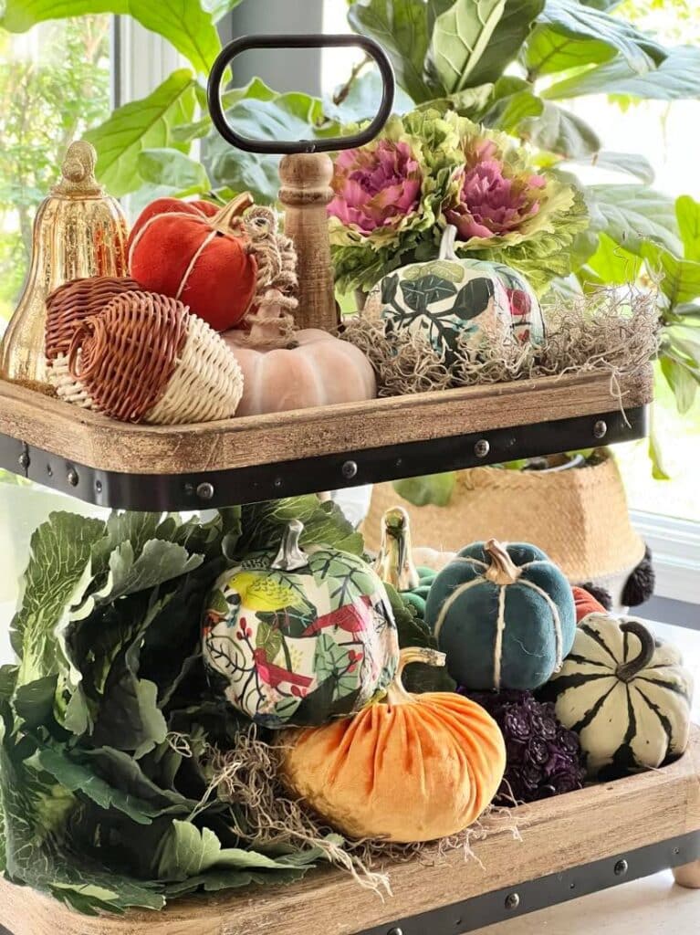 kitchen fall decor ideas: A wood tiered tray filled with faux pumpkins, greenery, and faux cabbages.