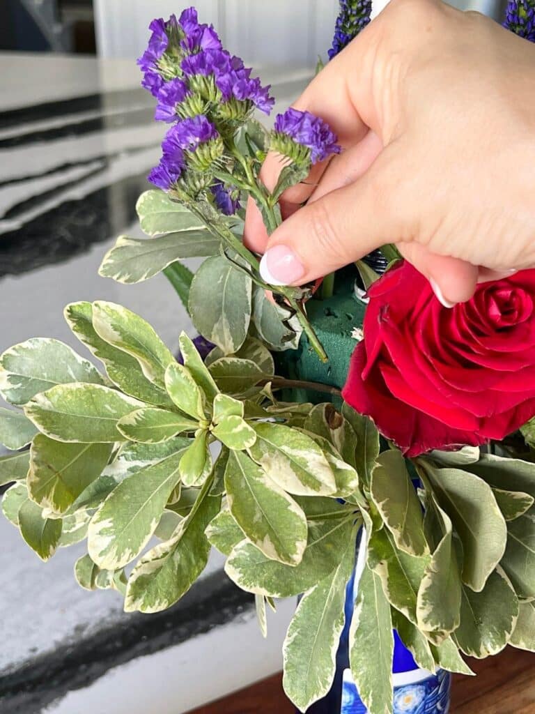 Adding a purple flower to the wine bottle with labels arrangement.