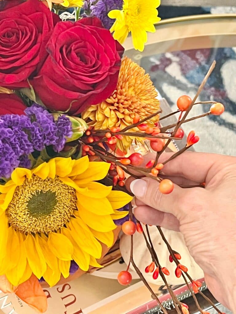 Arranging orange pip berries in pumpkin floral arrangements.