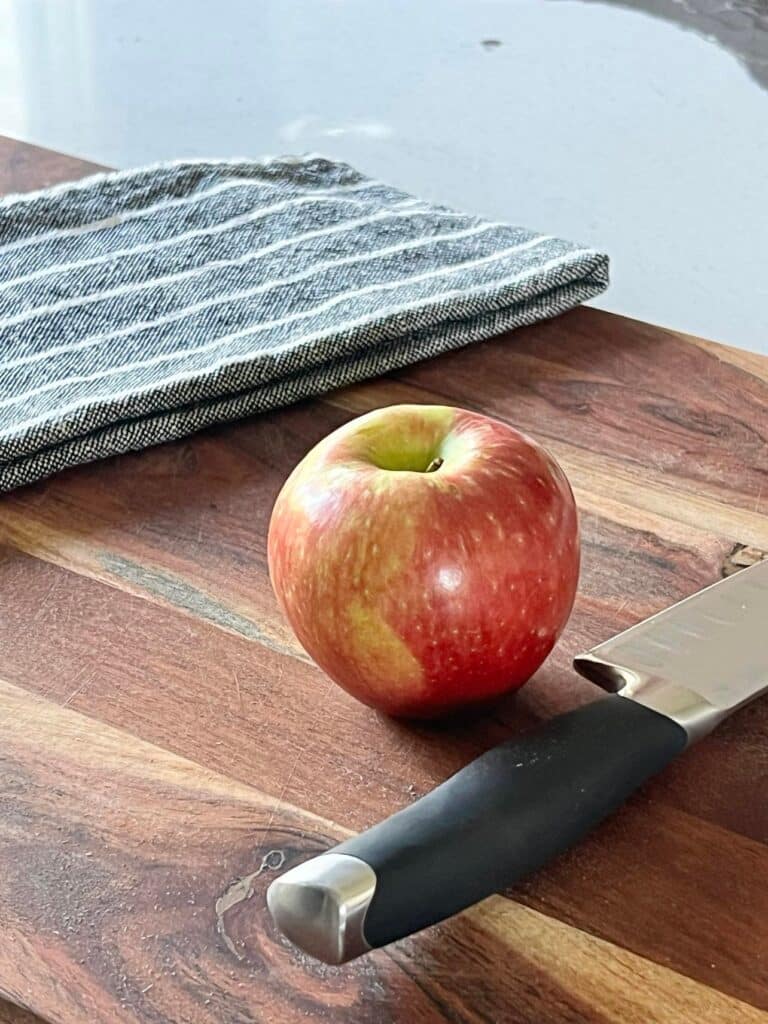 An apple on a wood cutting board.